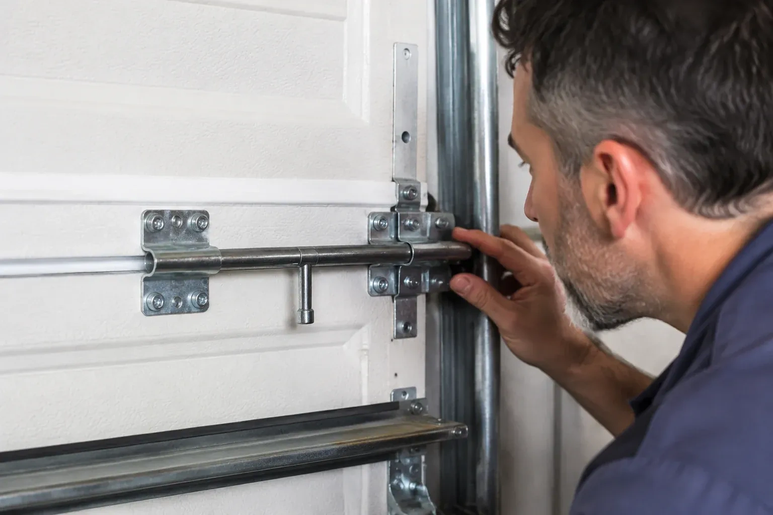Person leaning close to a white paneled door, one hand on a metal slide-bolt bar mounted across the panel. — Garage Door Manual Lock Repair, Vaughan