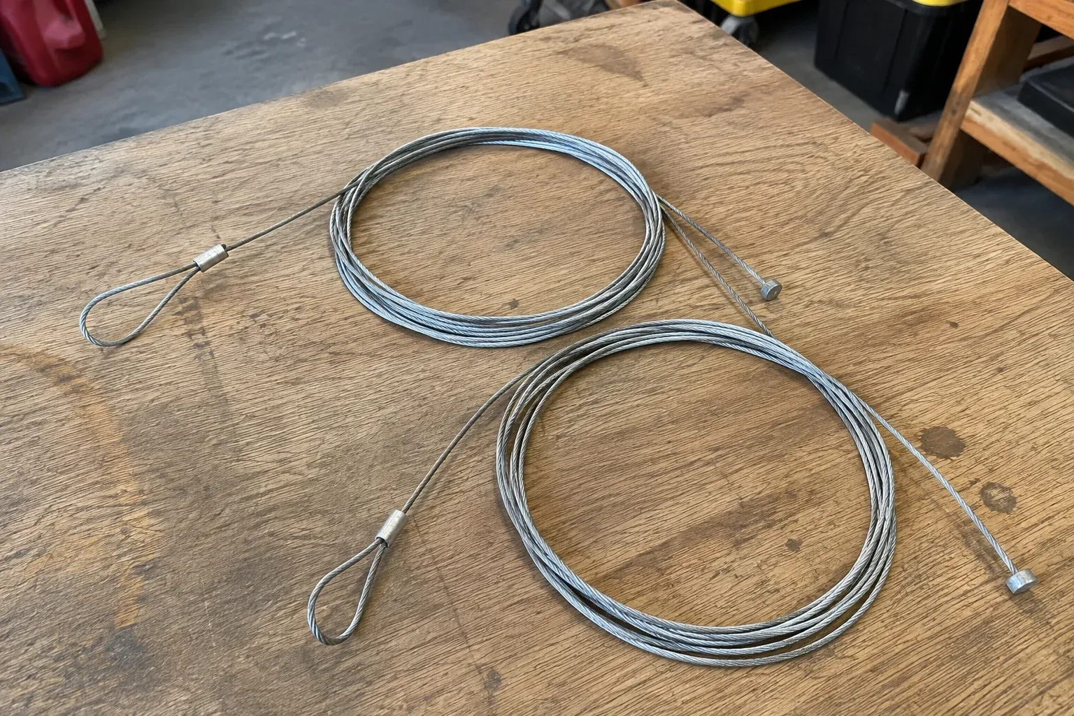 Two coiled steel cables with loop and stop ends on a workbench. — Garage Door Cable Replacement, Vaughan